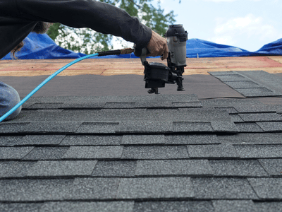 Professional roofer using nail gun to adhere shingles to the roof