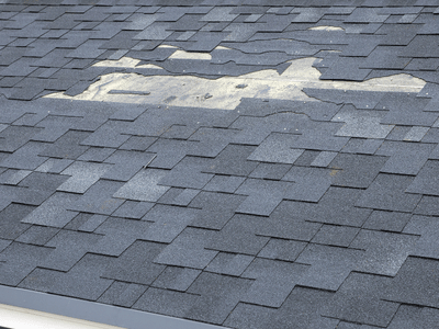 A roof with torn and missing asphalt shingles after storms damaged it