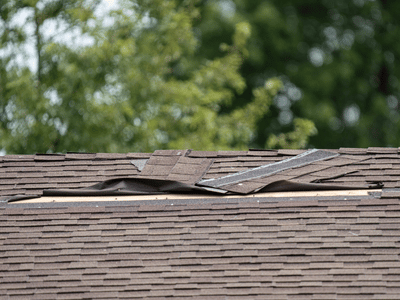 A roof with torn and curled shingles after storms damaged it