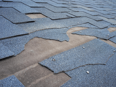 A roof with torn and missing asphalt shingles after storms damaged it